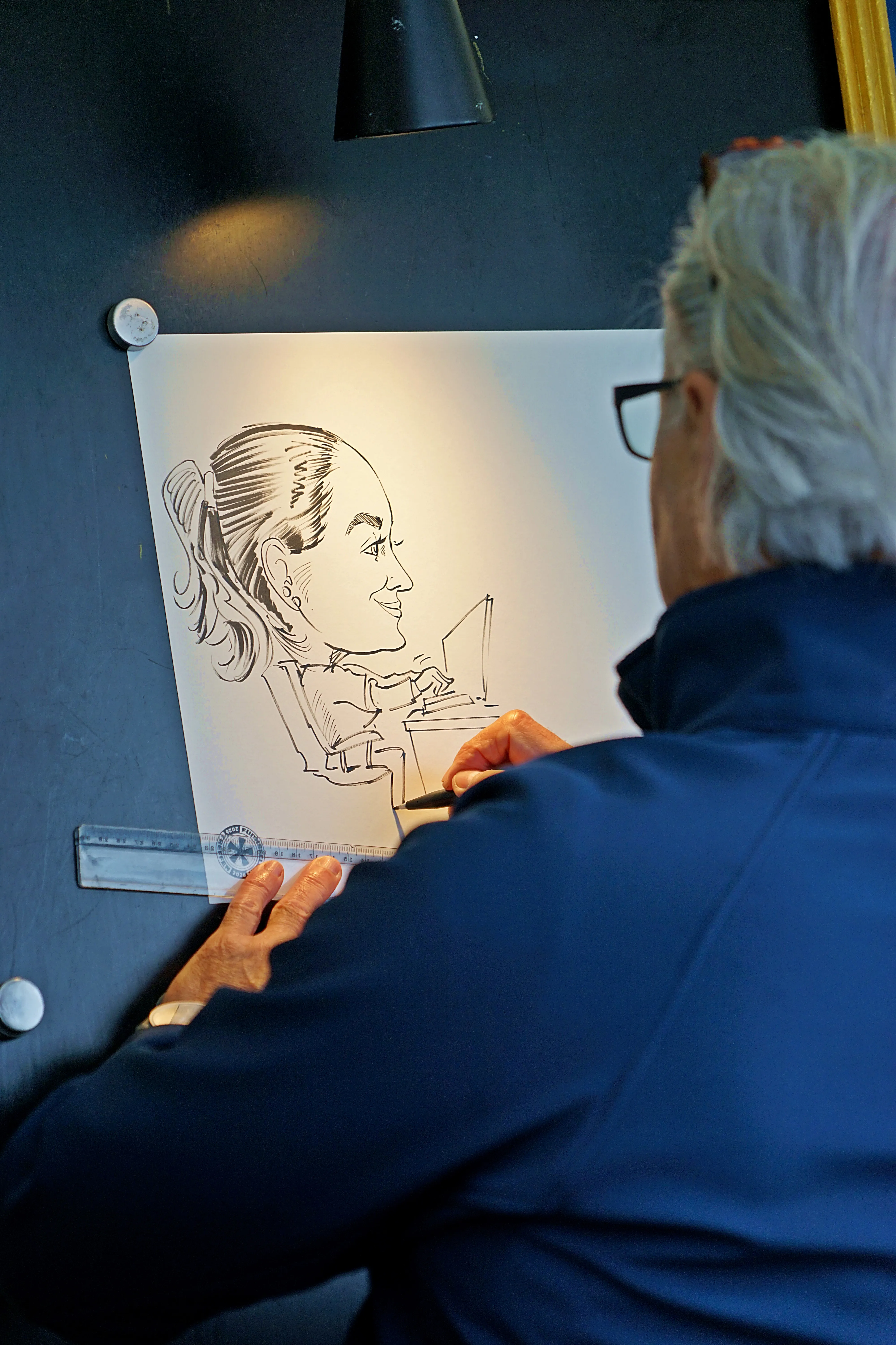 Ein Künstler zeichnet mit einem Stift die Karikatur einer lächelnden Frau, die an einem Laptop arbeitet.