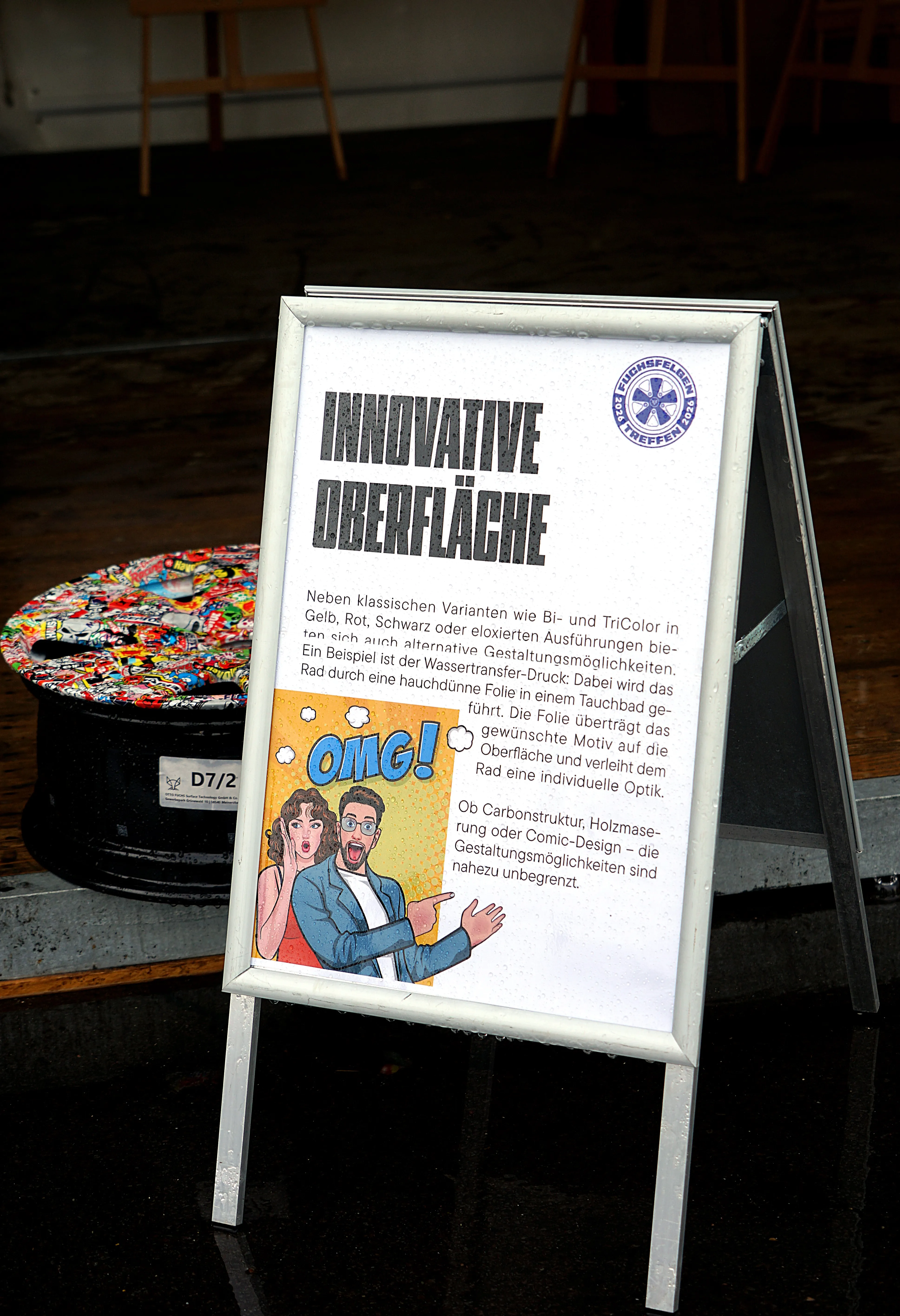 Werbetafel bewirbt innovative Oberflächengestaltung für Räder, illustriert mit Comicfigur und Rad mit buntem Muster.