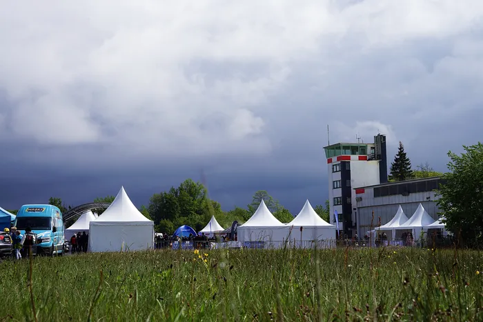 Ein Feld mit Wildblumen im Vordergrund, dahinter mehrere weiße Zelte und ein Kontrollturm unter einem bewölkten Himmel beim Fuchsfelgen-Treffen.
