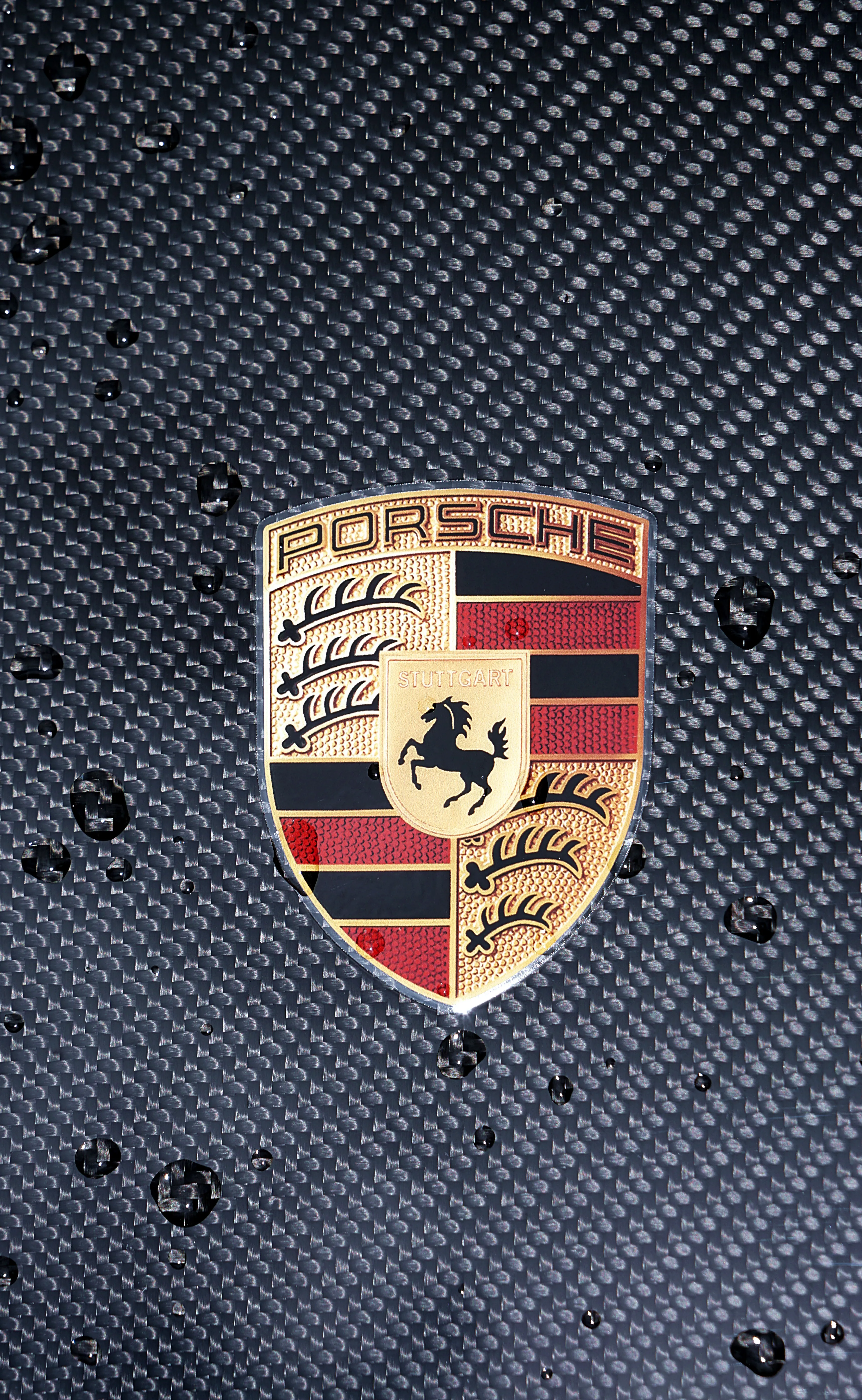 Porsche-Wappen auf einem strukturierten, dunklen Hintergrund. Das Logo zeigt ein rotes und goldenes Wappen mit einem springenden Pferd und der Aufschrift „Porsche“ und „Stuttgart“.