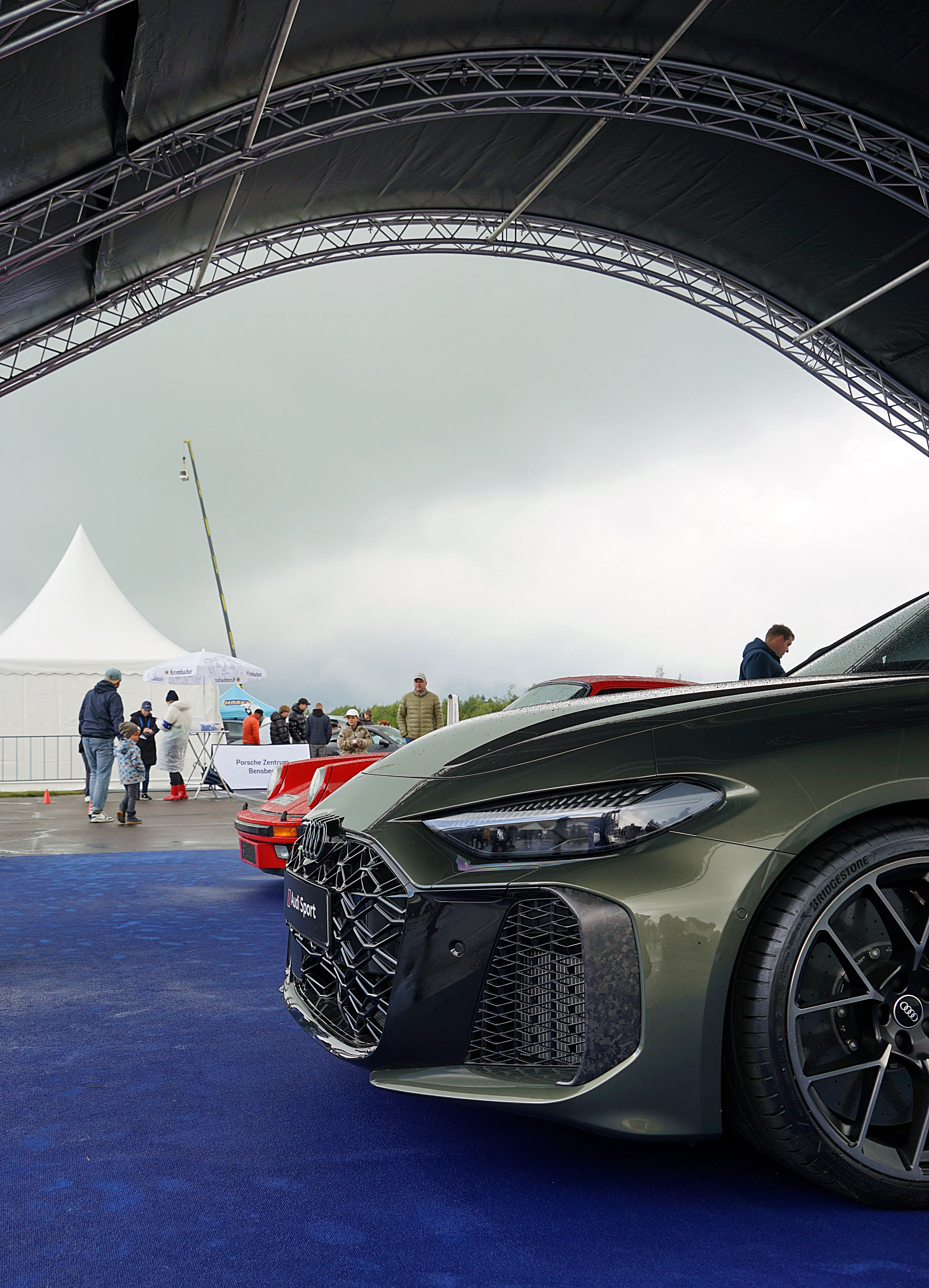 Dunkelgrüner Audi E-tron GT mit großen Rädern steht unter einem Zelt, im Hintergrund weitere Autos und Besucher des Fuchsfelgen-Treffens.