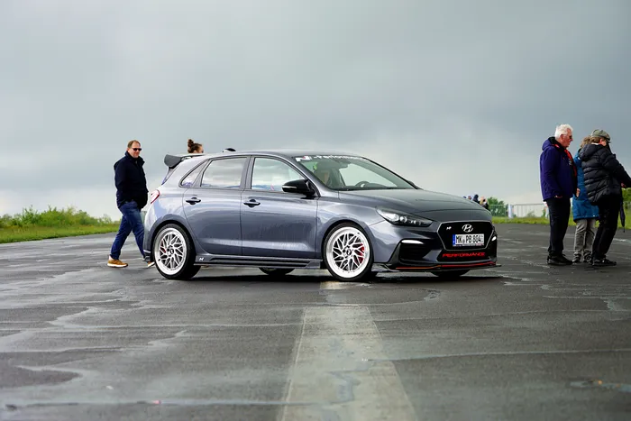 Grauer Hyundai i30 N mit Tuning-Elementen und auffälligen Felgen steht auf einem Asphaltplatz, umgeben von Zuschauern.