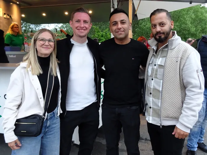 Vier Männer und eine Frau stehen eng zusammen und lächeln in die Kamera. Im Hintergrund ist ein Foodtruck und weitere Menschen zu sehen.