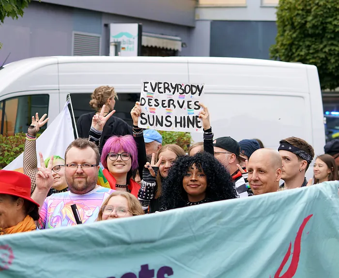 Teilnehmer des Christopher Street Day in Lüdenscheid halten ein Schild mit der Aufschrift „EVERYBODY DESERVES SUNSHINE“ hoch.