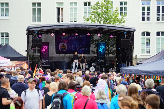 Zwei Personen stehen auf einer Bühne vor einer Menschenmenge beim Christopher Street Day in Lüdenscheid.