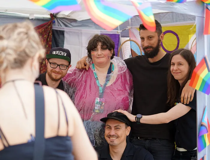 Eine Gruppe von Menschen posiert vor einer Kulisse mit Regenbogen-Wimpeln.