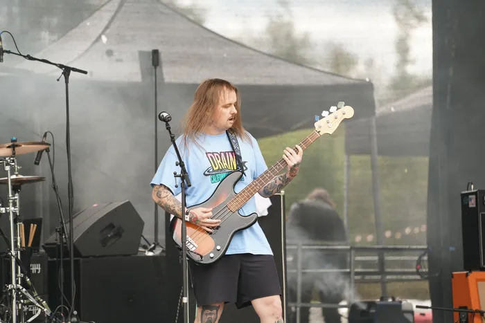 Ein Mann mit langen Haaren spielt eine Bassgitarre auf einer Bühne.