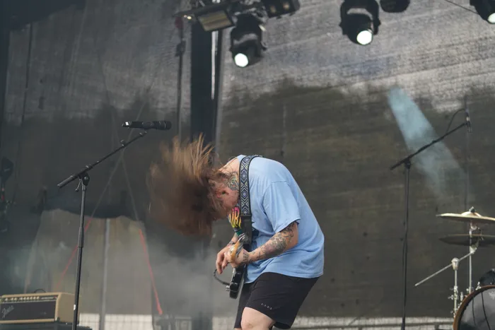 Ein Musiker mit langen Haaren spielt E-Gitarre und headbangt auf einer Bühne vor Bühnennebel.