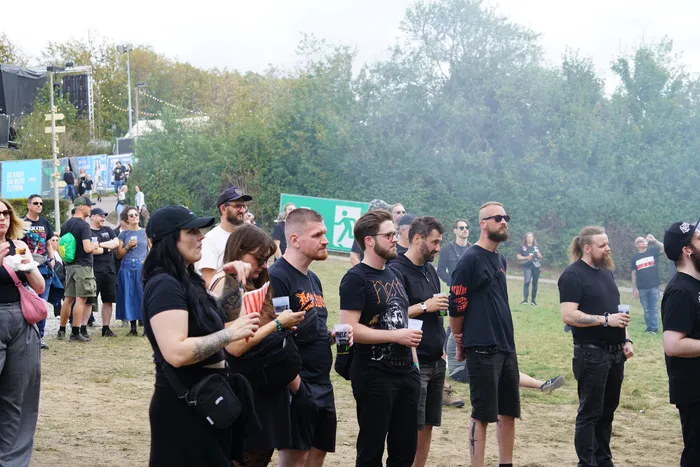 Eine Gruppe von Menschen steht bei einem Open-Air-Event auf einer Wiese vor Bäumen.