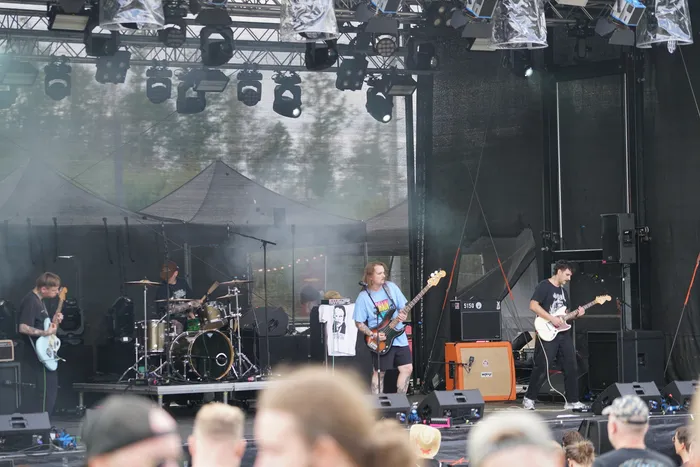Eine Rockband spielt mit Gitarren und Schlagzeug auf einer beleuchteten Außenbühne.