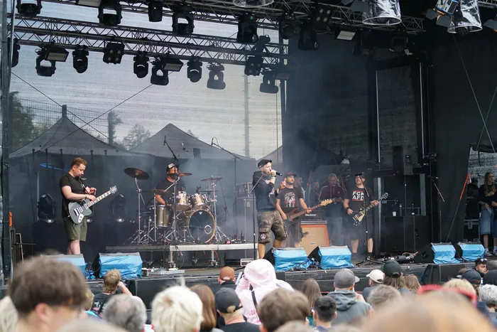 Eine Band tritt auf einer Außenbühne mit Schlagzeug und Gitarren vor einem Publikum auf.