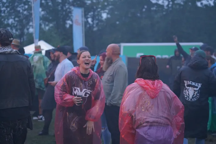 Eine lachende Frau in einem transparenten roten Regenponcho steht in einer Menschenmenge bei einem Open-Air-Festival.