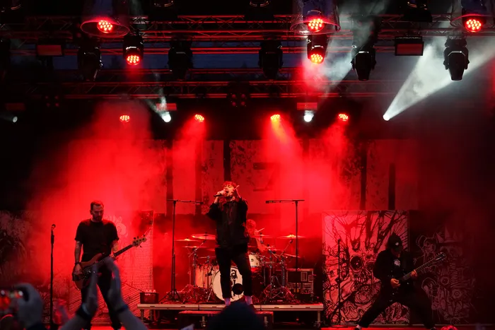 Die Band Callejon performt auf einer Bühne unter intensivem rotem Licht und Nebel vor grafischen Hintergründen.