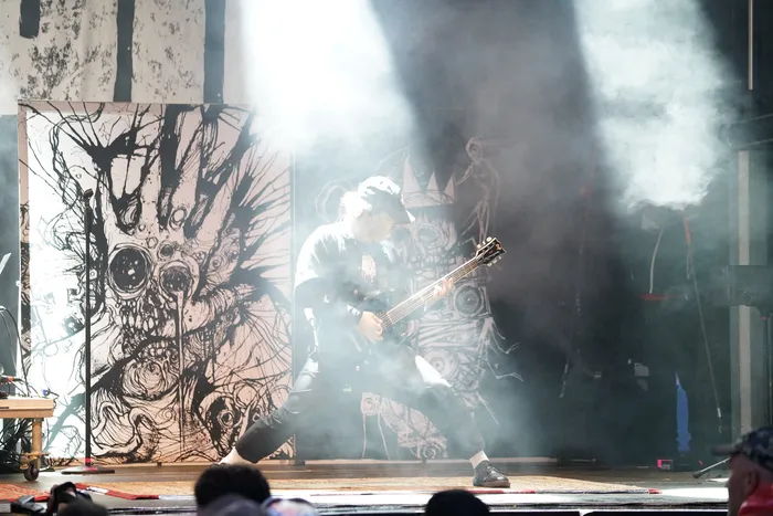 Ein Musiker spielt eine E-Gitarre auf der Bautz26 Collabo Stage vor einem großflächigen, illustrierten Hintergrund und dichtem Bühnennebel.