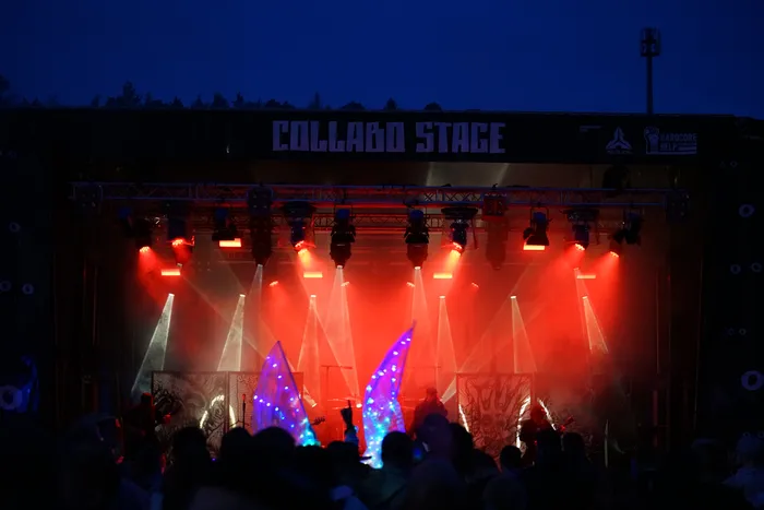 Die Collabo Stage wird mit roten und weißen Scheinwerfern beleuchtet, vor der eine Menschenmenge steht.