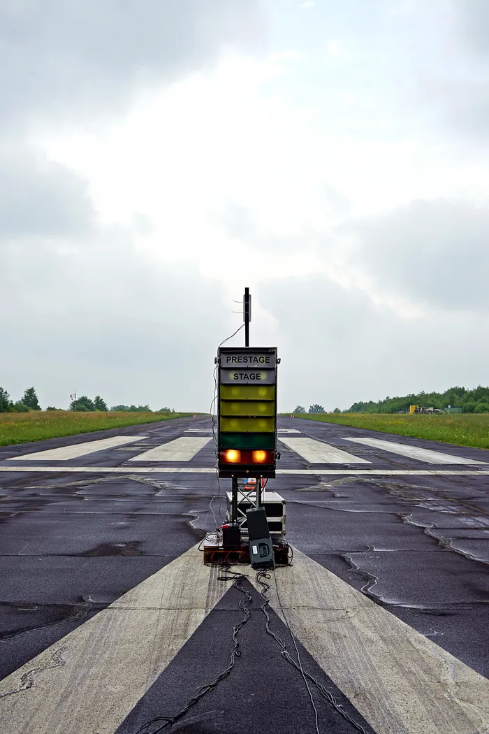 Eine Start- und Landebahn mit einem gelben Schild mit der Aufschrift „PRESTAGE“ und „STAGE“ darauf, umgeben von weißen Markierungen und unter einem bewölkten Himmel.