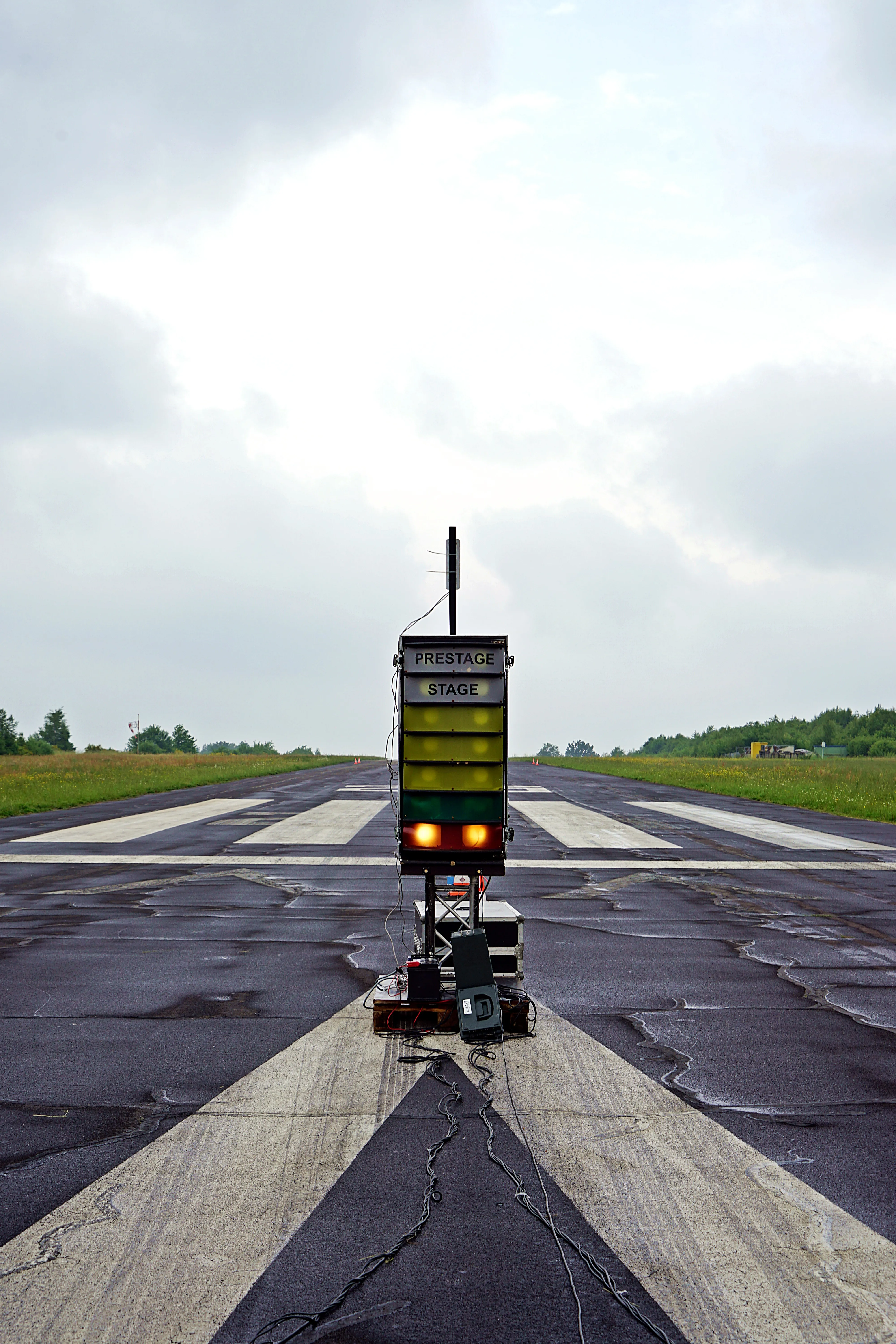 Eine Start- und Landebahn mit einem gelben Schild mit der Aufschrift „PRESTAGE“ und „STAGE“ darauf, umgeben von weißen Markierungen und unter einem bewölkten Himmel.