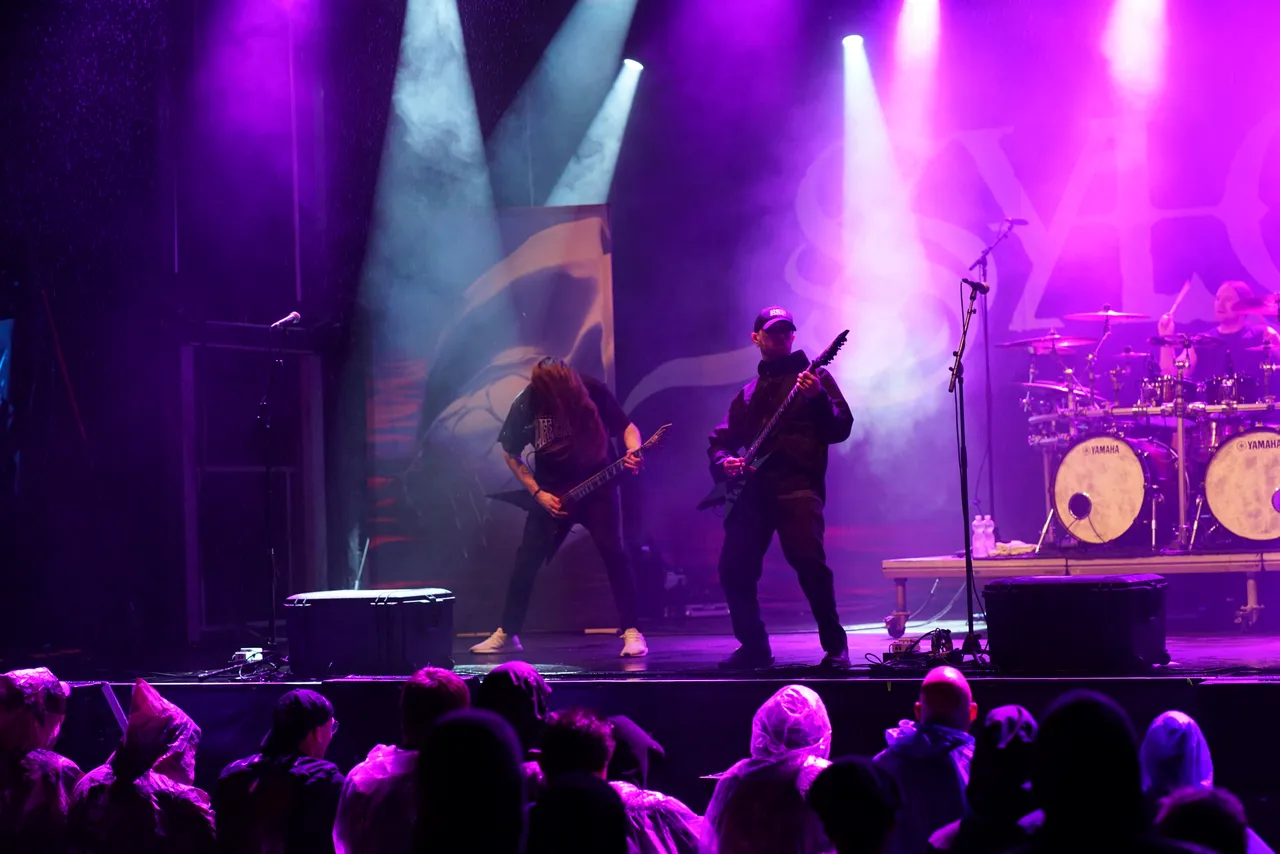 Zwei Gitarristen der Band Sylosis spielen unter violettem Bühnenlicht und Nebel auf einer Konzertbühne.