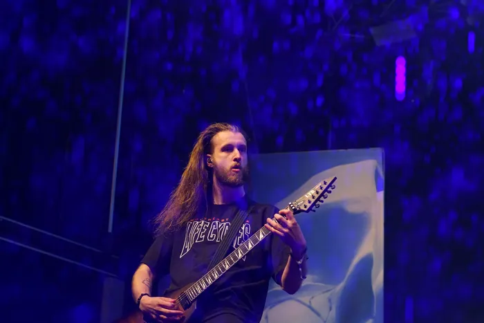 Ein Musiker der Band Sylosis spielt eine E-Gitarre auf einer blau beleuchteten Bühne.