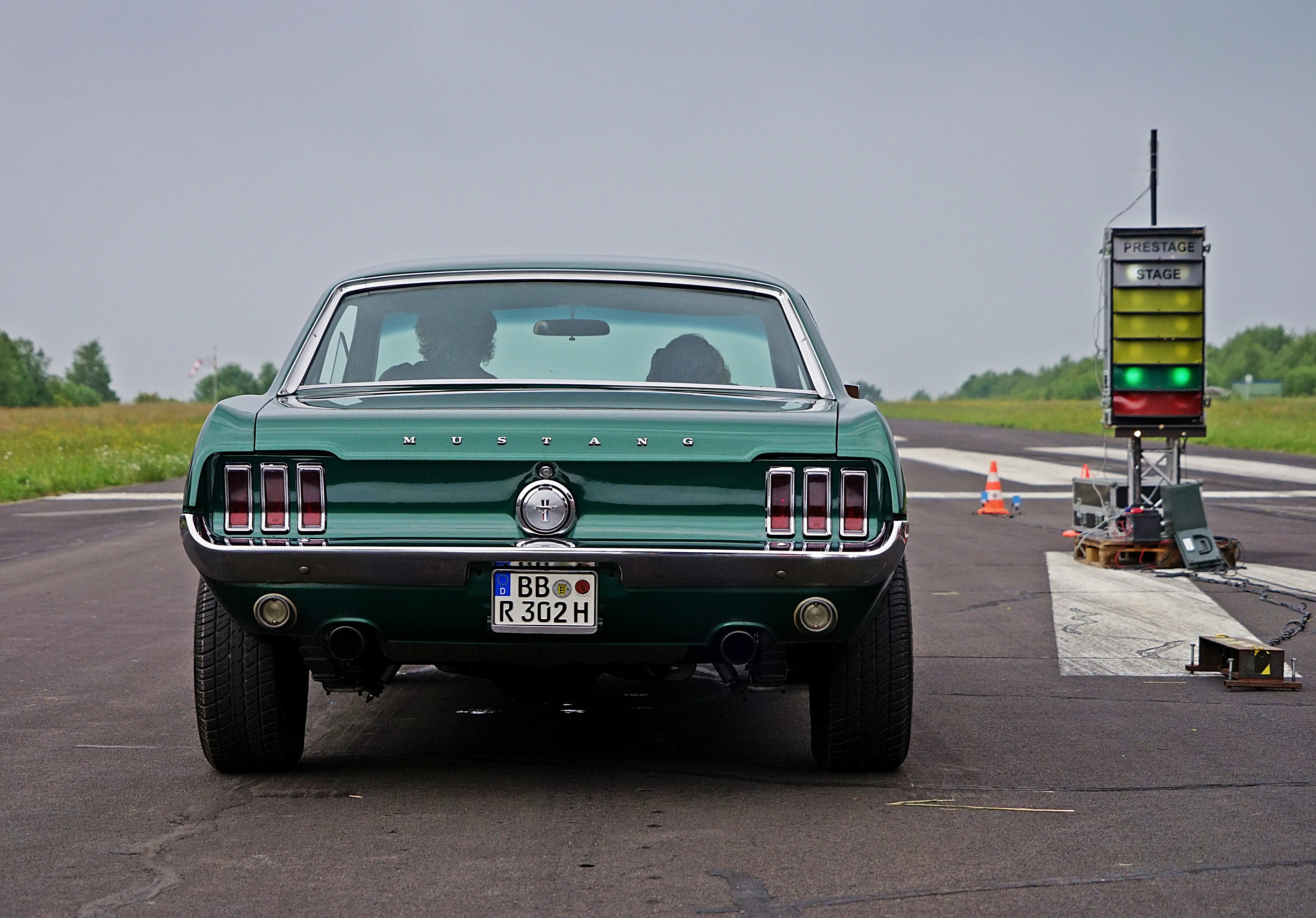 Grüner Ford Mustang steht auf einer Rennstrecke, bereit für den Start. Im Hintergrund eine Startampel und ein Feld.