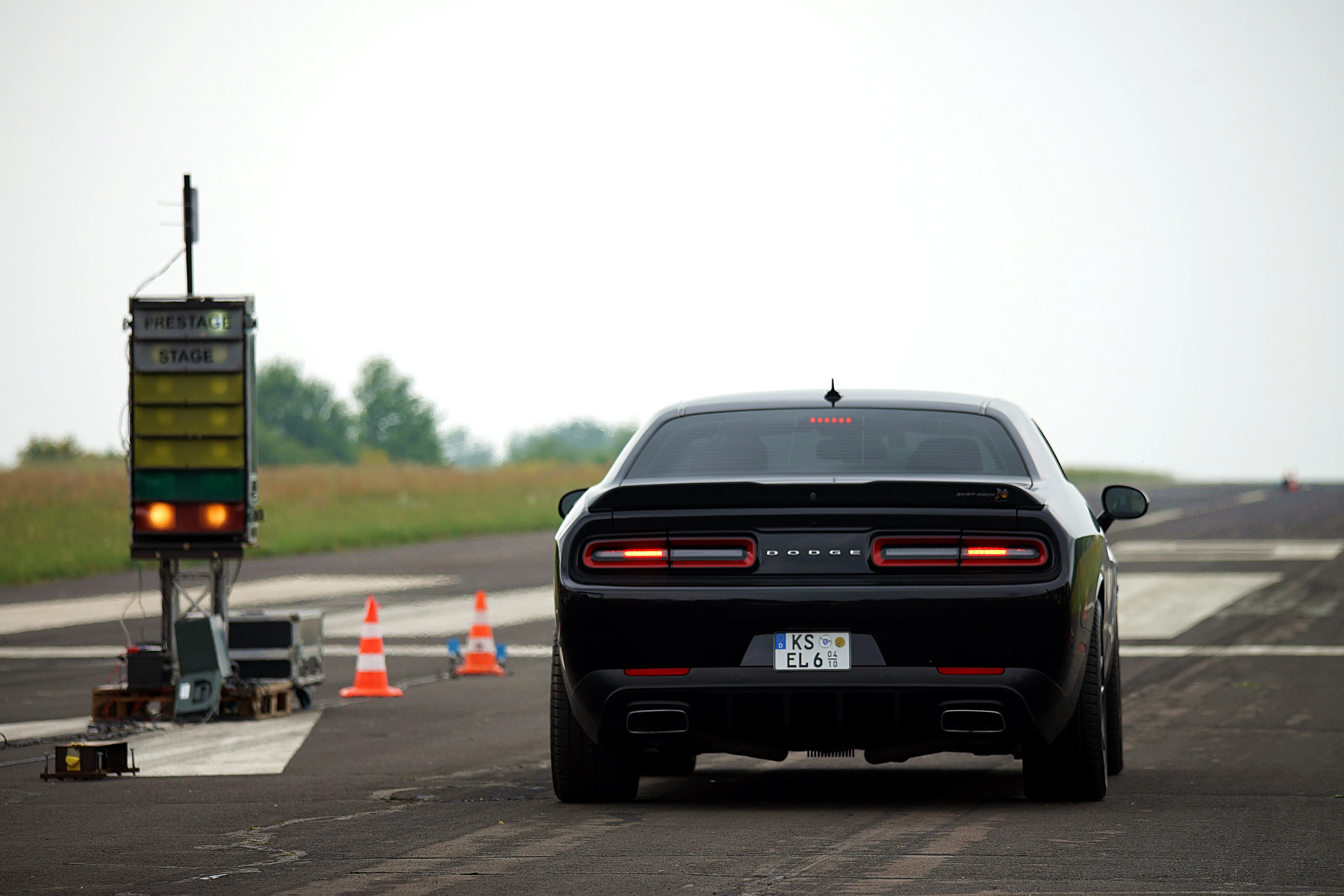 Schwarzer Dodge Challenger steht auf einer Rennstrecke vor einer Startampel, bereit für einen Beschleunigungslauf.