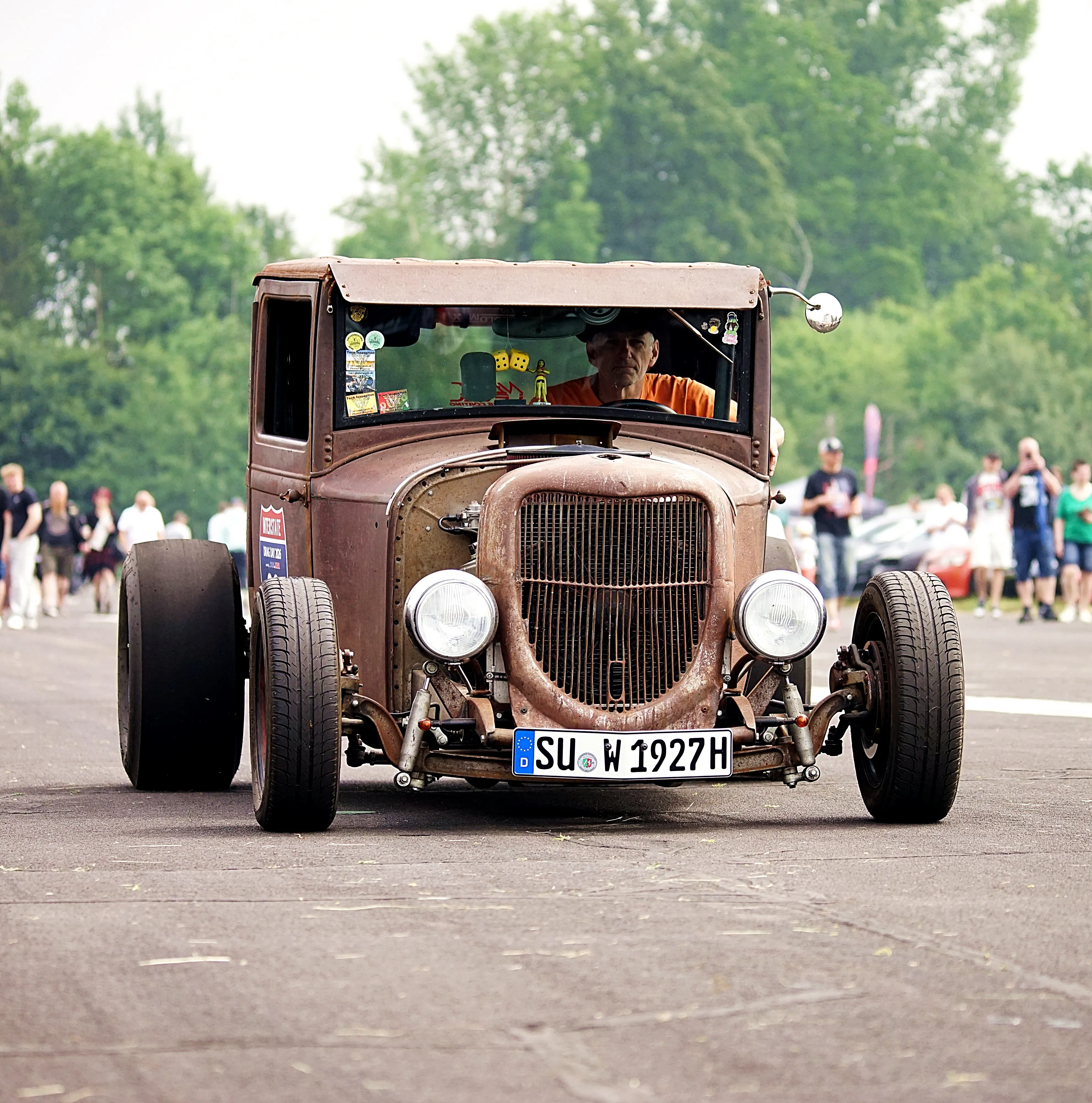 Rostbrauner Oldtimer mit offenem Motorraum fährt auf einer Straße vor einer Menschenmenge. Das Kennzeichen lautet SU-W 1927H.