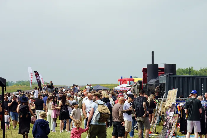 Große Menschenmenge auf einem Feld vor einem schwarzen Container mit einem Schornstein, vermutlich auf einem Festival oder einer Veranstaltung.
