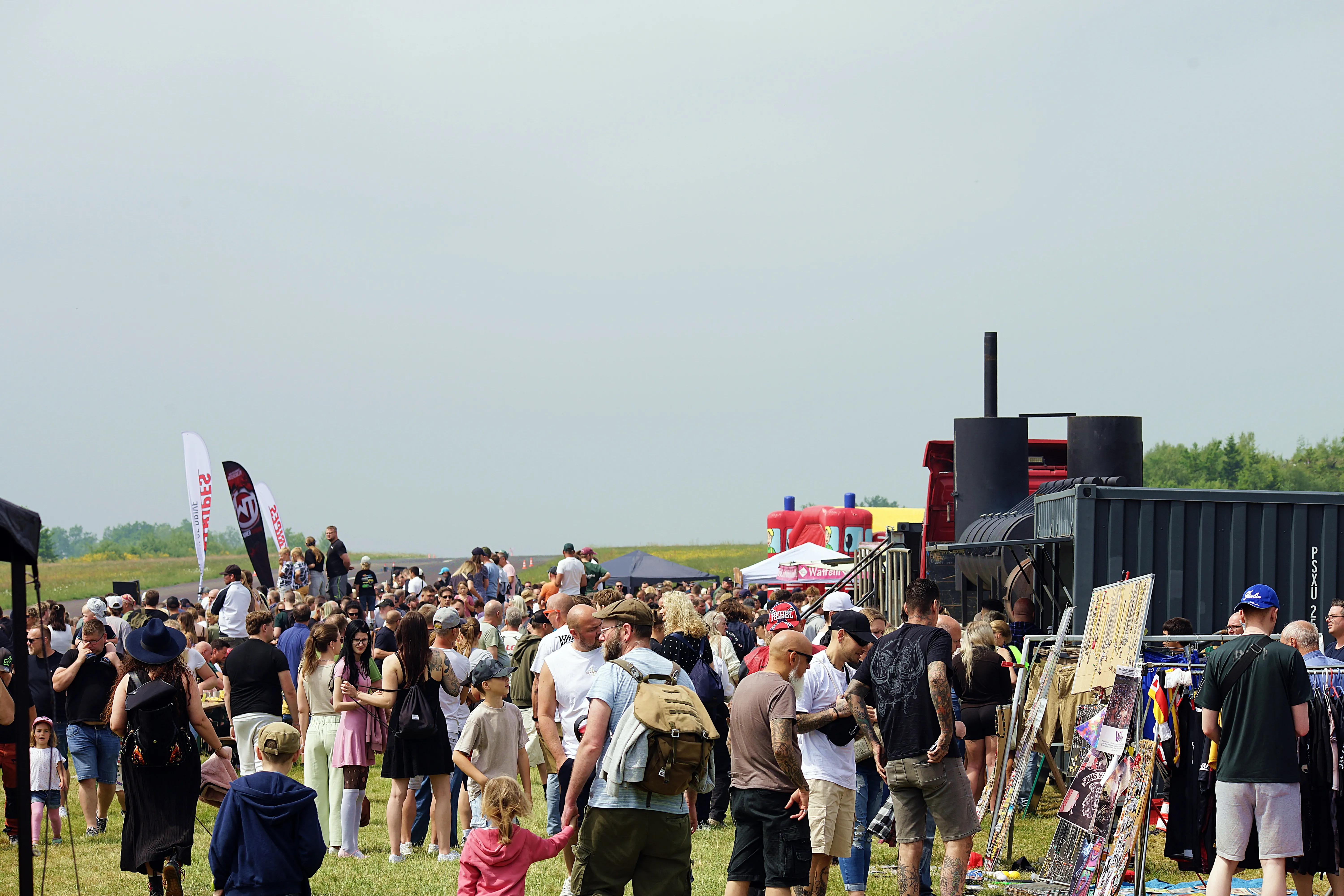Große Menschenmenge auf einem Feld vor einem schwarzen Container mit einem Schornstein, vermutlich auf einem Festival oder einer Veranstaltung.