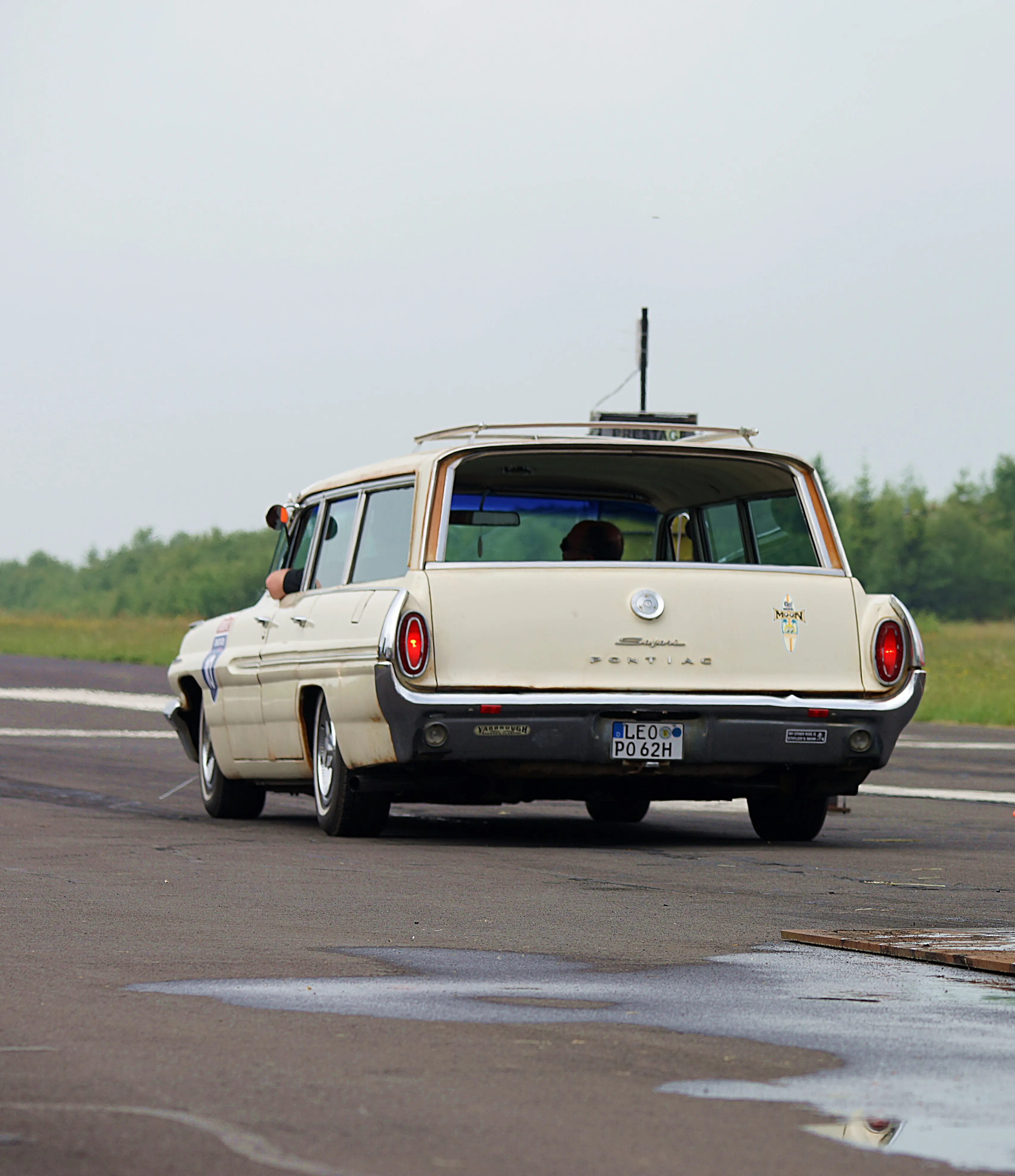 Beigefarbener Pontiac Station Wagon aus den 1960er Jahren mit Dachgepäckträger und Antenne auf einem Asphaltstreifen.