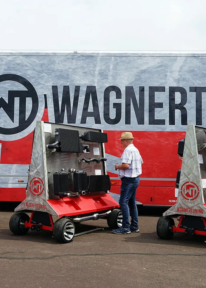 Ein Mann steht vor zwei roten Kühlwagen mit dem Logo von Wagner Tuning vor einem grauen LKW mit dem Schriftzug Wagner Tuning.