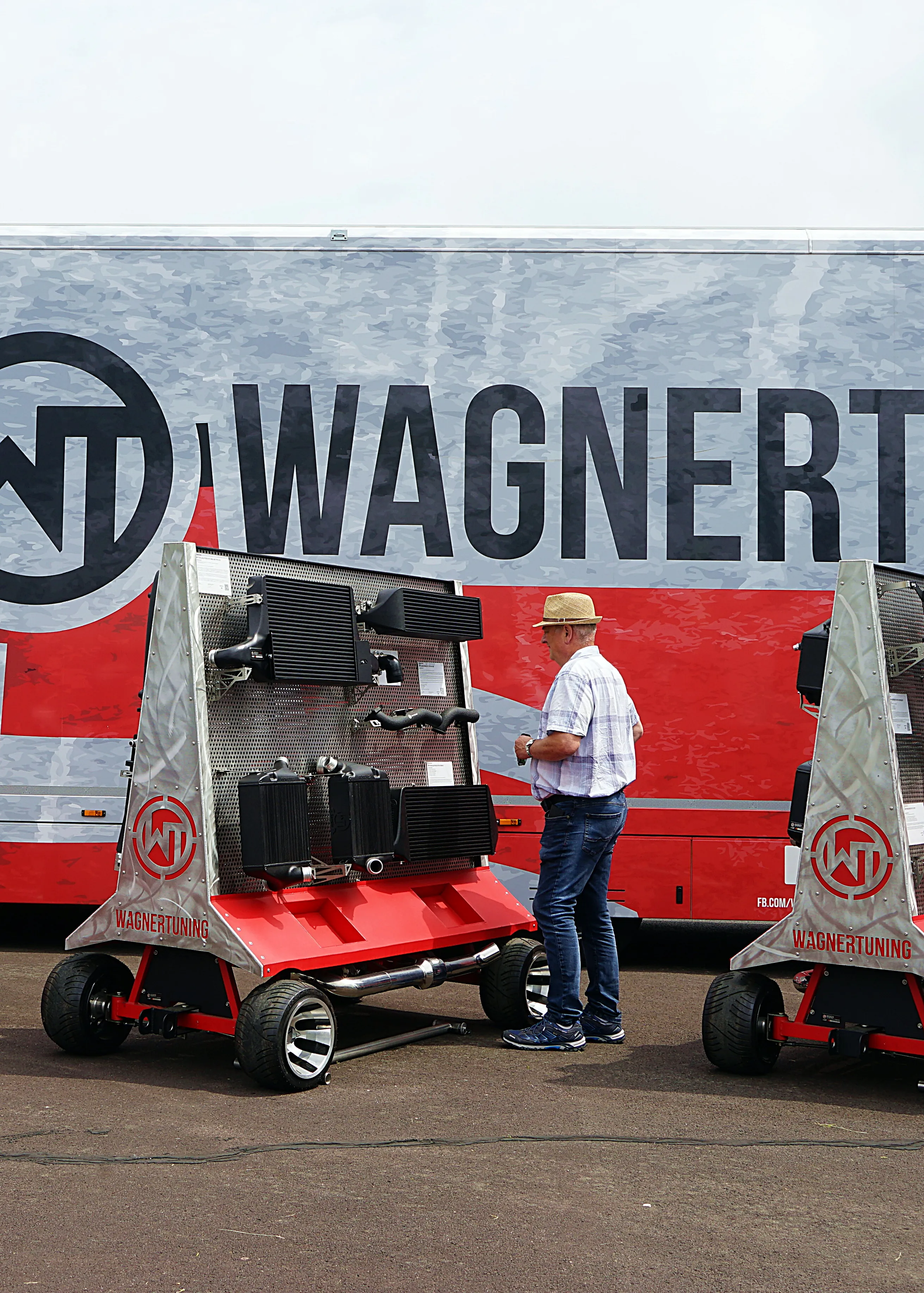 Ein Mann steht vor zwei roten Kühlwagen mit dem Logo von Wagner Tuning vor einem grauen LKW mit dem Schriftzug Wagner Tuning.