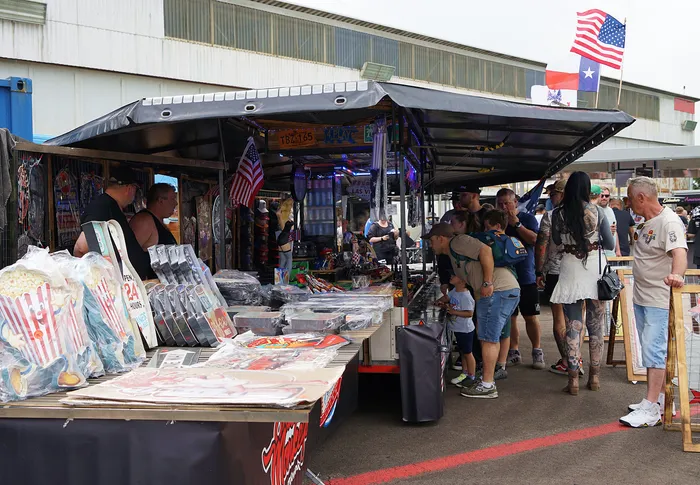 Ein belebter Marktstand mit Souvenirs, Sammelkarten und patriotischen Artikeln zieht eine vielfältige Besuchergruppe an.