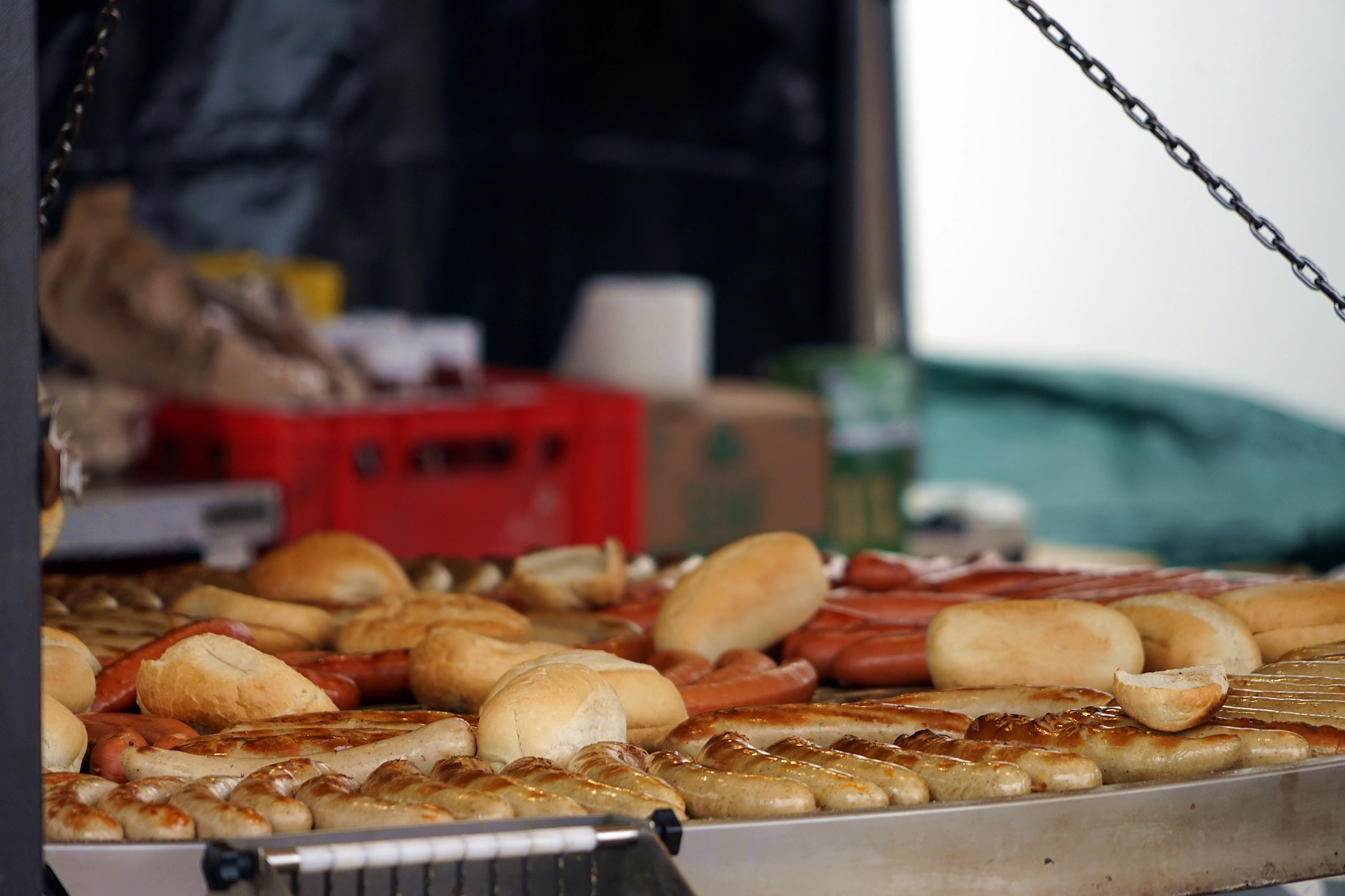 Grill mit verschiedenen Würsten und Brötchen, teilweise belegt, vor einem unscharfen Hintergrund.