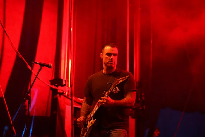Ein Musiker der Band Stick To Your Guns spielt unter rotem Bühnenlicht eine E-Gitarre.
