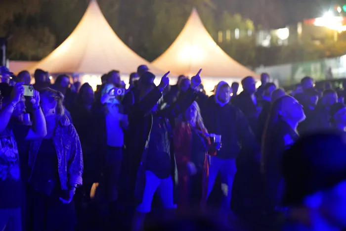 Menschenmenge bei einem Konzert vor zwei großen, beleuchteten Zelten unter blauem Licht.