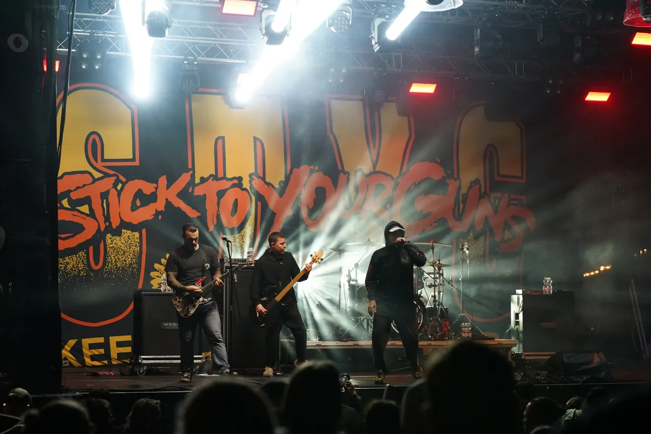 Die Band Stick To Your Guns tritt live auf einer hell beleuchteten Bühne vor einem großen Logo auf.