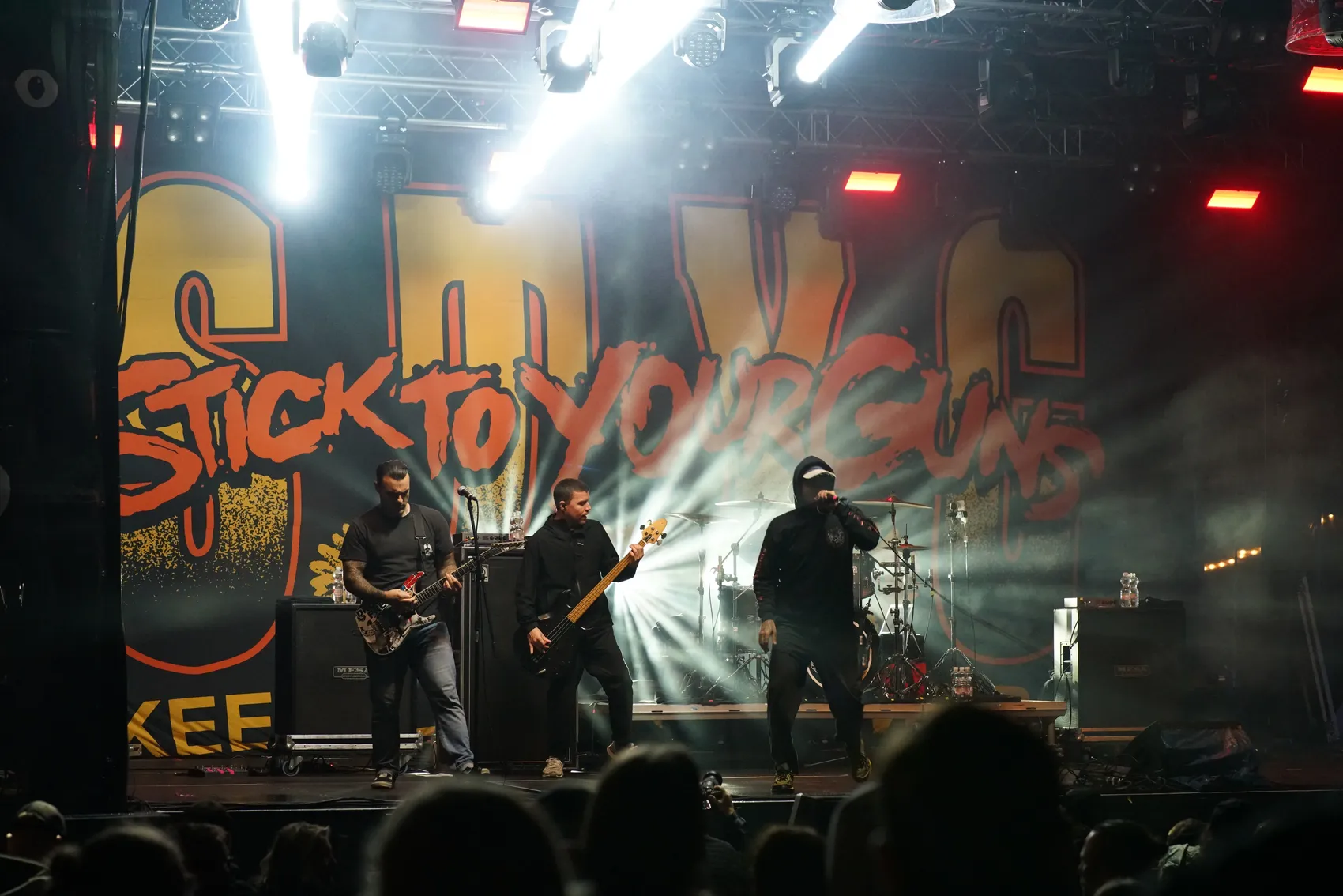 Die Band Stick To Your Guns tritt live auf einer hell beleuchteten Bühne vor einem großen Logo auf.