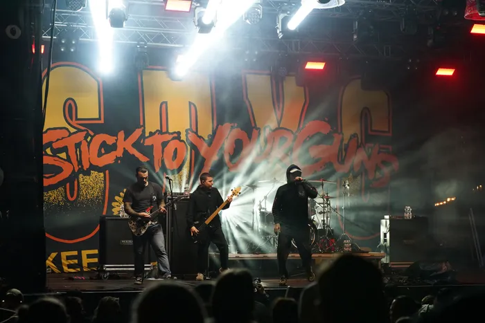 Die Band Stick To Your Guns tritt live auf einer hell beleuchteten Bühne vor einem großen Logo auf.