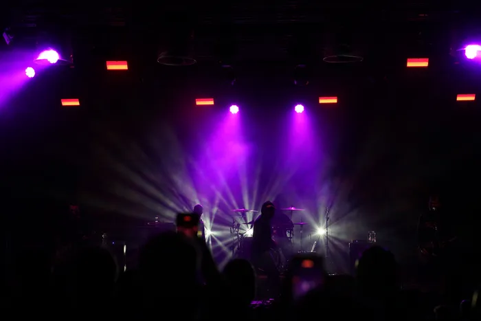 Musiker der Band Stick To Your Guns auf einer Bühne unter violetten Scheinwerferstrahlen vor einer Menge.