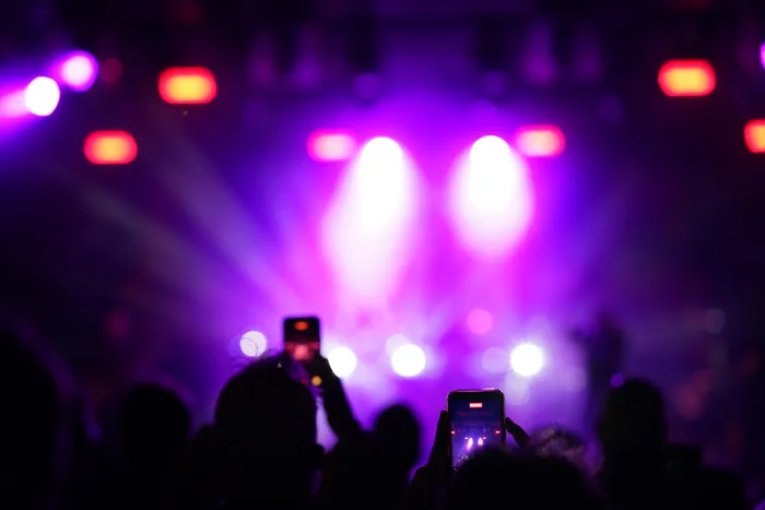 Silhouetten eines Publikums halten Smartphones hoch vor einer Bühne mit intensiven lila und pinkfarbenen Scheinwerfern.