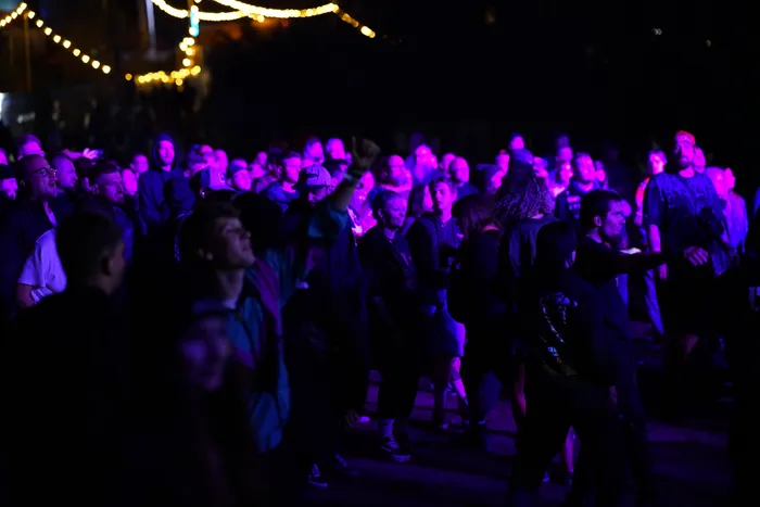 Eine Menschenmenge bei einem Konzert, beleuchtet von violettem Licht vor einer Lichterkette im Hintergrund.