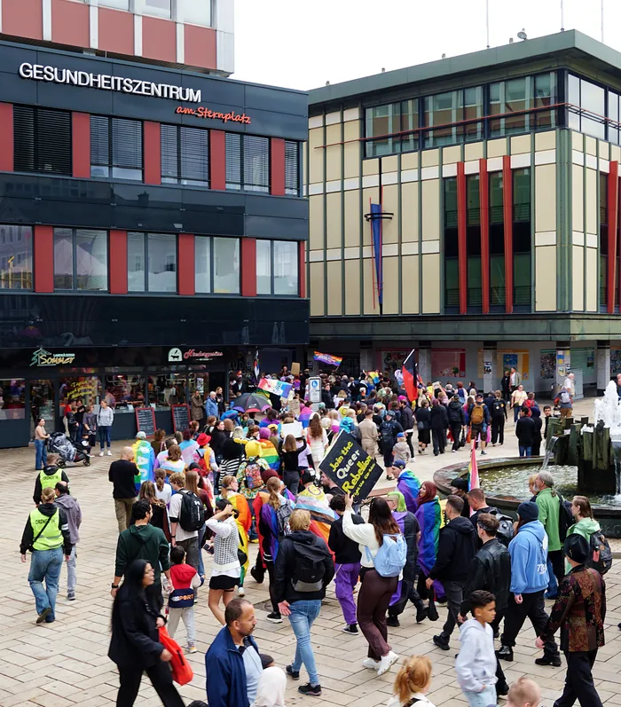 Eine Menschenmenge mit Regenbogenfahnen auf dem Sternplatz vor einem Gesundheitszentrum.