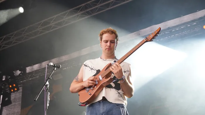 Ein Musiker spielt eine hellbraune E-Gitarre auf einer Bühne unter Scheinwerferlicht und Nebel.