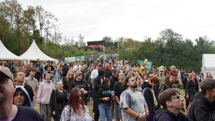 Eine große Menschenmenge versammelt sich bei einem Open-Air-Event vor weißen Zelten und Bäumen.
