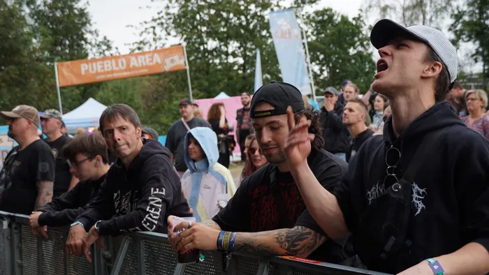 Menschenmenge an einem Absperrgitter bei einem Musikfestival, im Vordergrund ein junger Mann mit Kappe, der singt oder ruft.