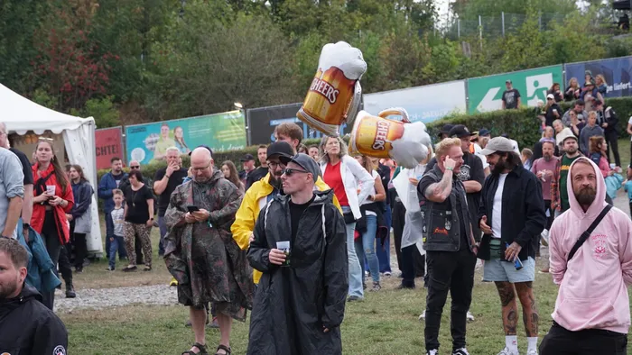 Menschenmenge bei einem Open-Air-Event mit großen, überdimensionierten Bierkrügen mit der Aufschrift „CHEERS“.