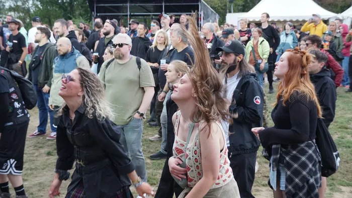 Eine lächelnde Frau mit blonden Locken blickt nach oben vor einer Menschenmenge bei einem Open-Air-Event.