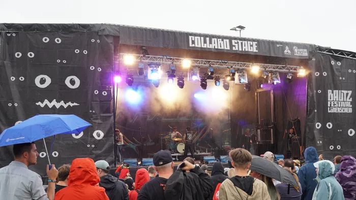 Musiker treten auf der „Collabo Stage“ beim Baltz Festival vor einer Menschenmenge unter hellen Scheinwerfern auf.