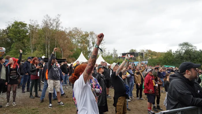 Eine Menschenmenge bei einem Open-Air-Event hebt die Hände und Fäuste in die Luft.