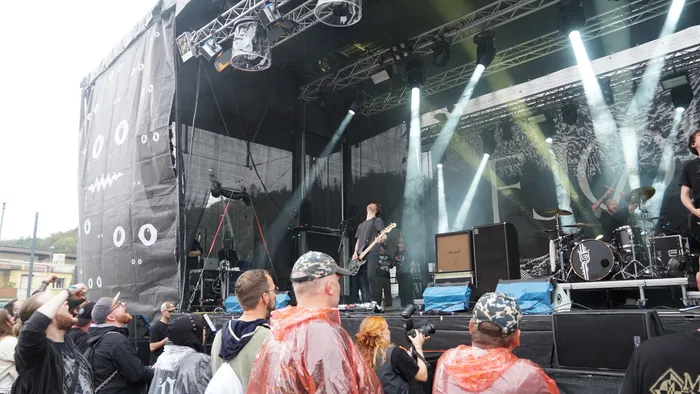 Eine Band spielt auf einer Bühne mit hellen Scheinwerfern vor einer Menschenmenge.